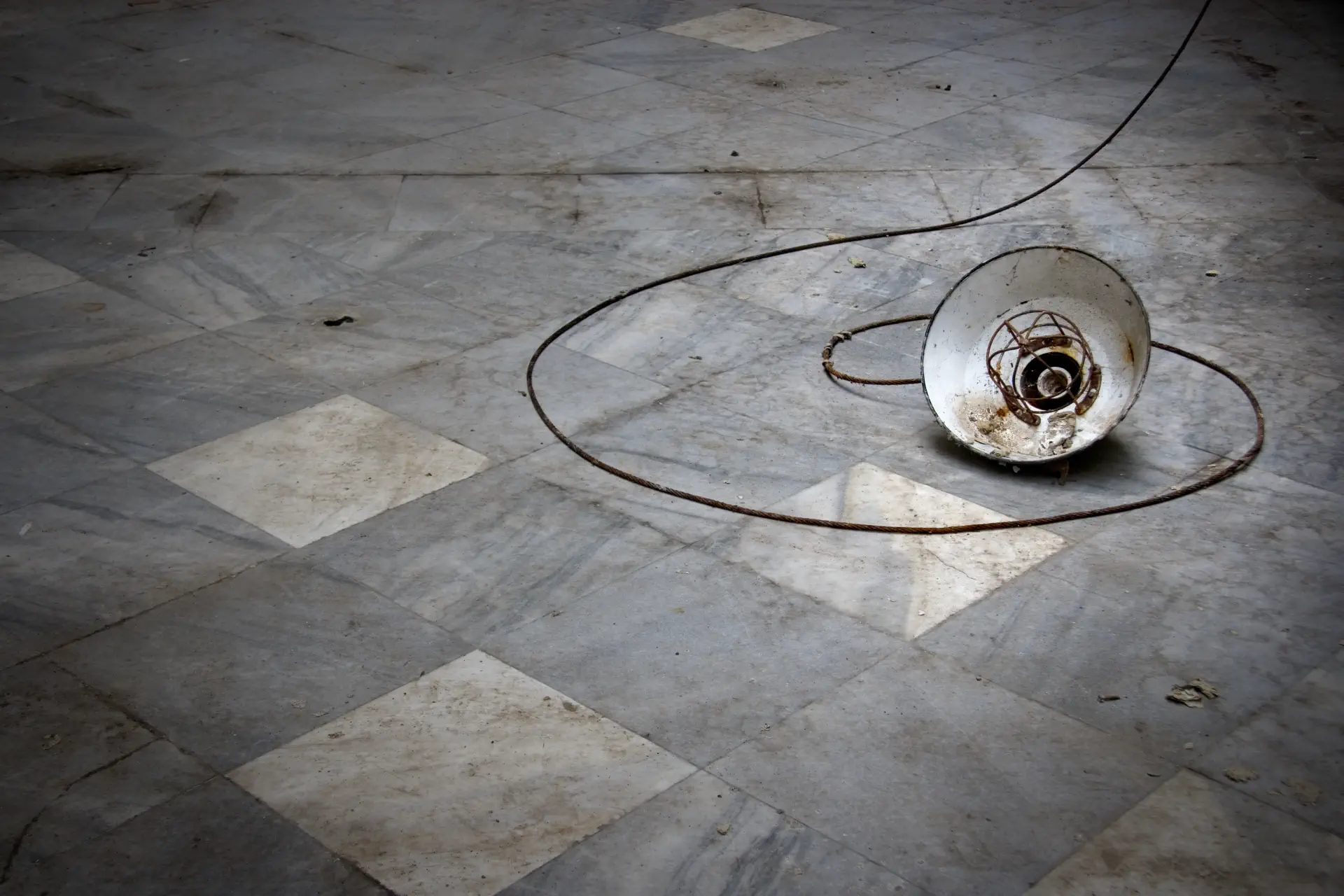 A broken lamp is lying on the ground, its cord wound up in a spiral shape.